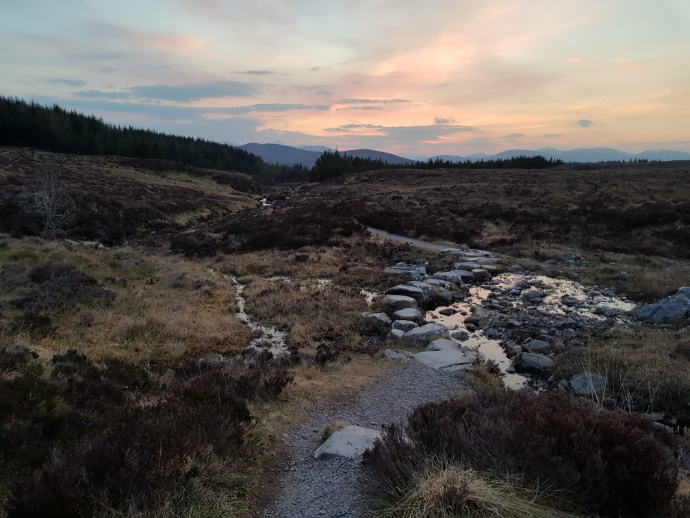 Path with stepping stones across a moorland stream, mountains in the distance